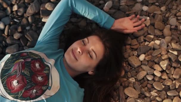 Nice, pretty woman lies with a smile on her face on a rocky beach in a sweetshot — Stock Video