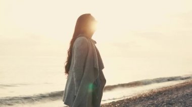 Gün batımında sahilde yürüyen bir kadın.