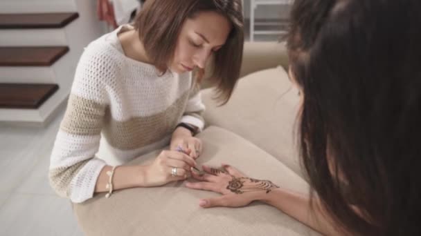 Mulher qualificada está desenhando padrões decorativos em mãos femininas por henna — Vídeo de Stock