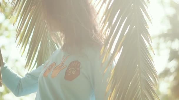 Дівчина-підліток з темним волоссям йде сонячною алеєю з долонями, крупним планом — стокове відео