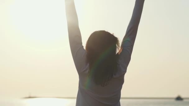Jonge slanke vrouw is stretching handen permanent tegen zonsopgang over zee — Stockvideo