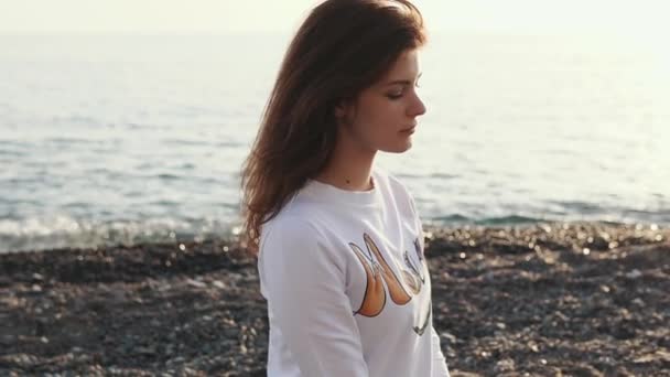 Brunette woman is relaxing alone on a gravel beach of sea in evening — Stock Video
