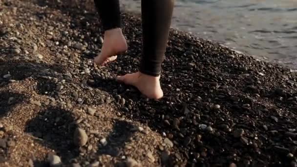 Gambe scalze di sottile giovane donna stanno scavalcando la spiaggia di ghiaia vicino all'acqua di mare — Video Stock