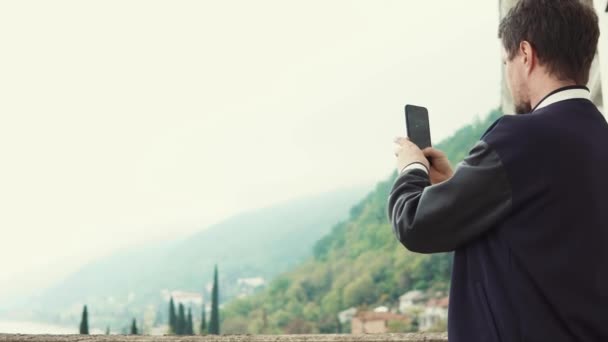 Man is het nemen van foto's en video door zijn telefoon van landschap, staande op het balkon — Stockvideo