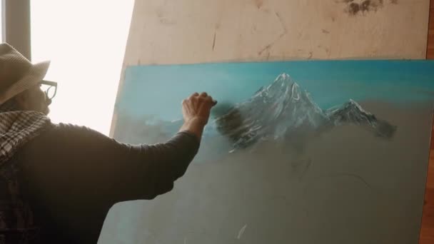 Old artist is drawing by white pastel mountains on a canvas — Stock Video