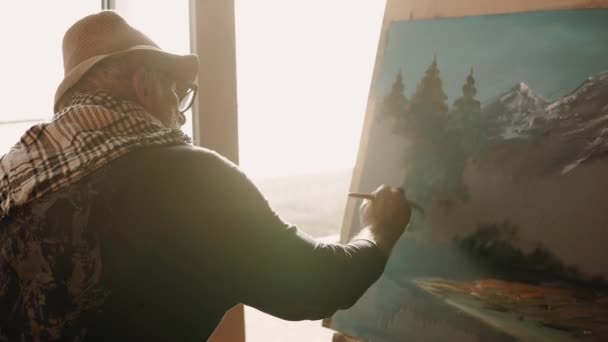 Alter einsamer Maler malt in seiner Werkstatt ein Bild mit Landschaft — Stockvideo