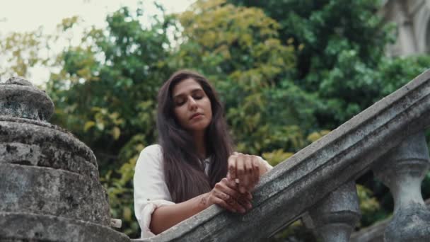 Femme romantique est debout près des mains courantes en pierre dans un jardin dans la journée — Video