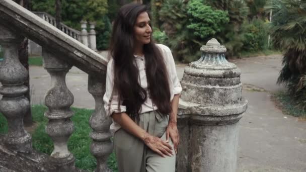 Cheerful pretty girl is standing in garden in old park in background of stair — Stock Video
