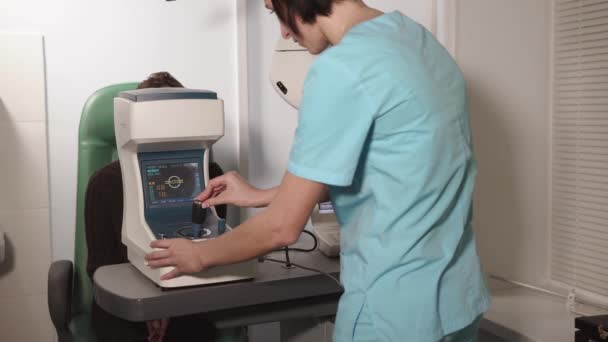 Врач, работающий офтальмологом, регулирует авторефрактометр для лечения зрения — стоковое видео