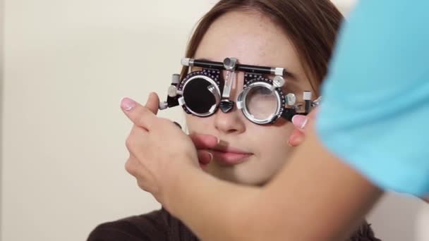 Oftalmólogo se está probando lentes en una montura de ensayo en la cara de la mujer — Vídeo de stock