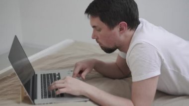 adam yatakta bir dizüstü bilgisayar ile.