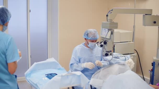 外科医生正在对病人的身体进行手术干预 两名医务人员的妇女正把无菌工具放在餐桌上看医生 — 图库视频影像