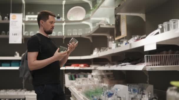 Uomo è in piedi in una zona di vendita del negozio di articoli da tavola e tenendo due bicchieri — Video Stock