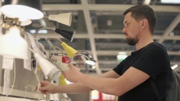 Jeune homme inspecte les lampes dans un magasin, en choisissant pour lui-même, gros plan — Video