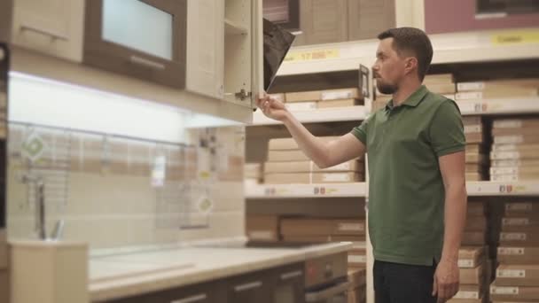 Homem está examinando mostra da cozinha moderna em uma loja de construção — Vídeo de Stock
