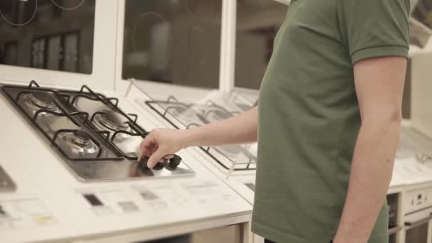 Чоловік обертається ручками виставкової панелі для приготування їжі в магазині, крупним планом — стокове відео