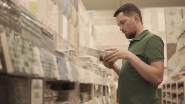 Hombre comprador está inspeccionando catálogo de productos de baldosas para trabajos de acabado en casas — Vídeo de stock