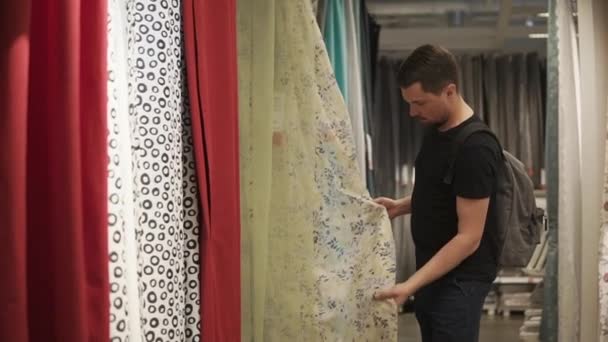 L'uomo sta scegliendo tende, sensazione di tessuto ed esaminando i colori in un negozio — Video Stock