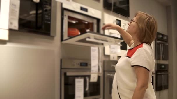 Retired woman is looking on ovens in retail shop, opening doors — Stock Video