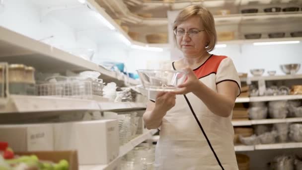 Bývalý žena se dívá na skleněná mísa ve svých rukou v obchodě nádobí