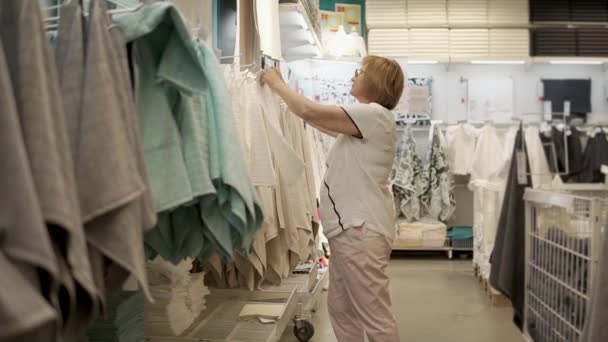 La anciana se siente y comprueba la toalla en una tienda, en una zona comercial — Vídeo de stock
