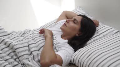 Yalnız esmer kadın yatak odasında yatağın kenarında oturan sabah uyanıyor