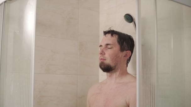 Homem de cabelos escuros está relaxando em um chuveiro à noite, de pé sob fluxos de água — Vídeo de Stock