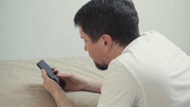 Adam ev yatakta yatan bir dokunmatik ekran smartphone, sayfalarında kaydırma