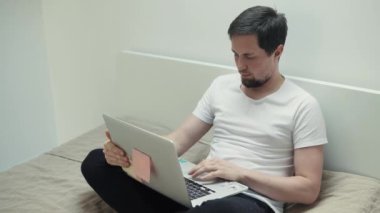 Brunet adam yatakta oturuyor ve akşam ev içinde laptop ile çalışma