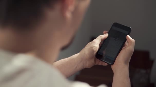 Guy está assistindo fotos em exibição de seu smartphone moderno, visão traseira — Vídeo de Stock