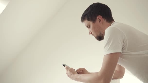 Alleen man is surfen op internet met behulp van zijn moderne smartphone op kamer — Stockvideo