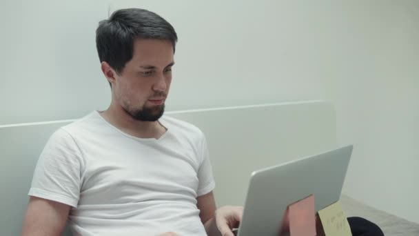 Компьютерщик работает в доме с ноутбуком, сидит на кровати — стоковое видео
