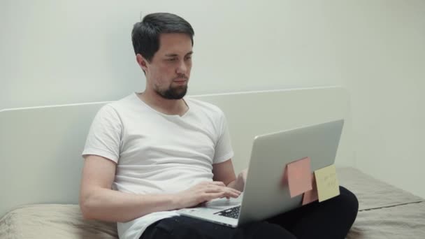 Человек заходит на интернет-сайты, пользуется ноутбуком, сидит в спальне — стоковое видео