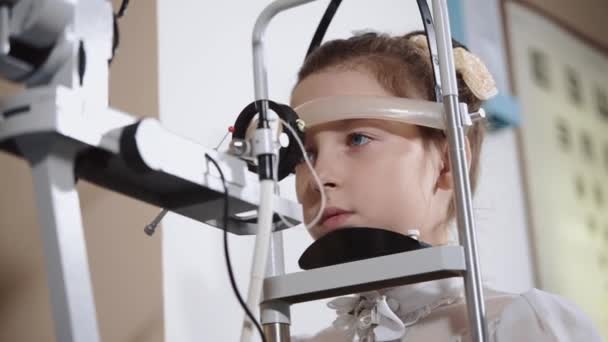 Menina está sentada calmamente na inspeção oftalmológica com cabeça fixa — Vídeo de Stock