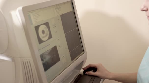 El médico está sentado detrás del dispositivo para la tomografía de la retina — Vídeos de Stock