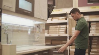 Genç bir adam kapıyı mutfak raf inceler ve satın almak için seçtiği