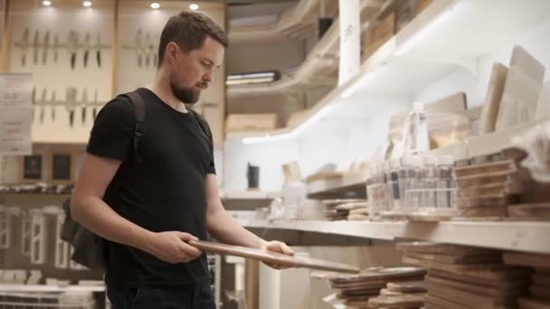 A young man picks a cutting board in the store in order to cook food on it — Stock Video