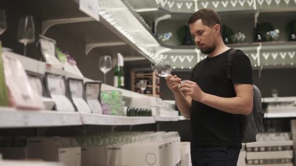 Een jonge man kiest voor zijn nieuwe appartement mooie glazen in het winkelcentrum — Stockvideo