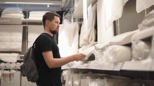 A young man looks at the sheet he wants to put in his apartment on the bed — Stock Video