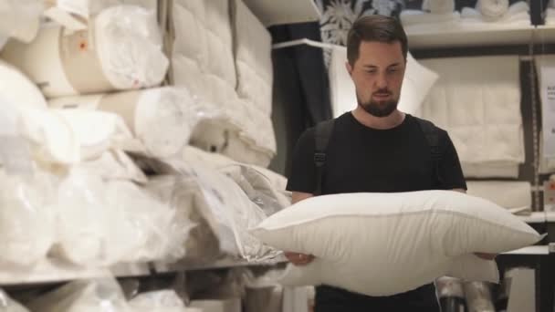 Młody człowiek patrzy na poduszce, chce wybrać niezbędne miękkość — Wideo stockowe
