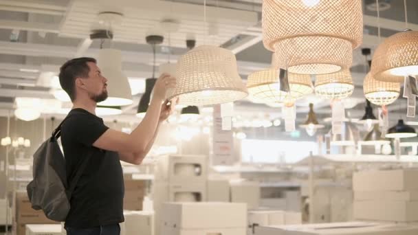 Дорослий чоловік, який знаходиться в магазині, розглядає торговельні лампи для ламп — стокове відео