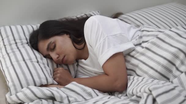 Una giovane donna sdraiata in un letto, con la testa su un cuscino, dorme — Video Stock