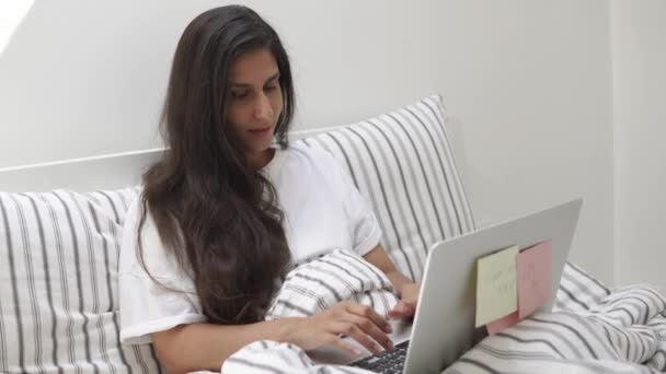 Jovem e bonita mulher está digitando texto no laptop deitado na cama em seu quarto — Vídeo de Stock