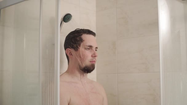 Porträt eines Mannes, der mit ernstem Blick unter der Dusche im Badezimmer steht — Stockvideo