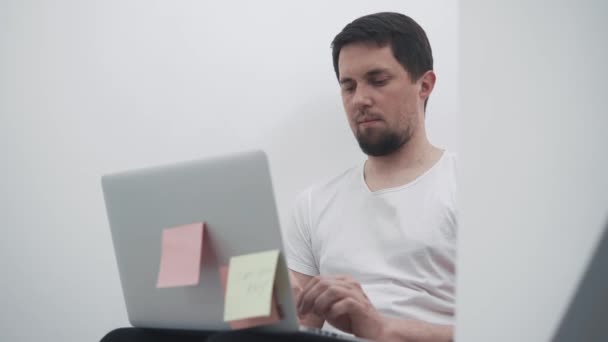 Молодой офисный работник сидит перед ноутбуком и разрабатывает новый проект — стоковое видео