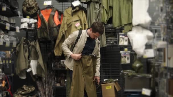 Adult man is examining trousers in a shop of clothes for hiking and fishing — Stock Video