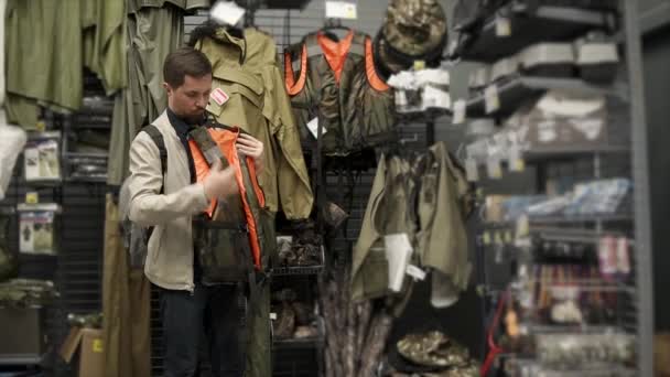 Νέοι γενειοφόρος άνδρας είναι σχετικά με ένα σωσίβιο γιλέκο του χώρου των πωλήσεων σε ένα κατάστημα για ψάρεμα — Αρχείο Βίντεο