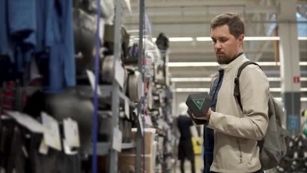 Bebaarde man houdt halter in een hal van sport winkel, controle van gewicht — Stockvideo