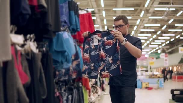 Shopper sostiene la percha con pantalones cortos brillantes en las manos y se aplica a su cuerpo — Vídeos de Stock