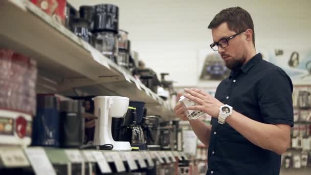 Junger Mann mit Brille begutachtet eine Tasse Kaffeemaschine in einer Ladenhalle — Stockvideo